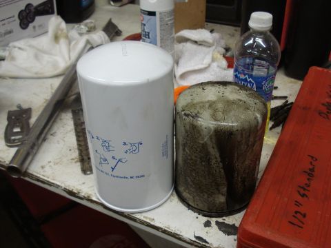 1989 Ford F-250 - Comparing a new oil filter to a used one on a workbench with various tools and supplies.