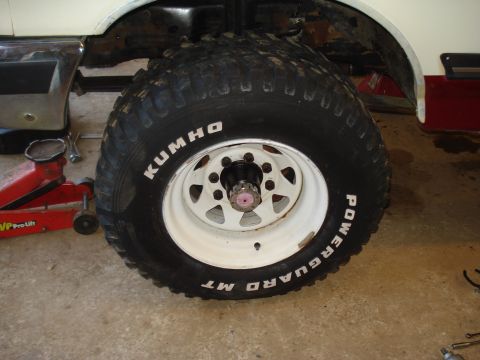 1989 Ford F-250 - A Kumho Powerguard MT tire is mounted on a white rim, with the vehicle's frame and a red jack visible.