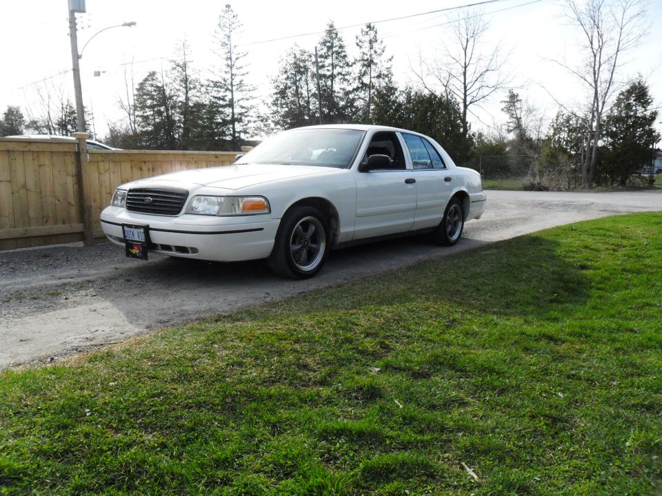 White Ford Crown Victoria sedan parked on a gravel driveway