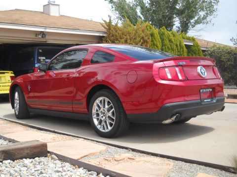 2012 Ford Mustang - Rear view of a red Ford Mustang coupe parked in a driveway next to a yellow vehicle.