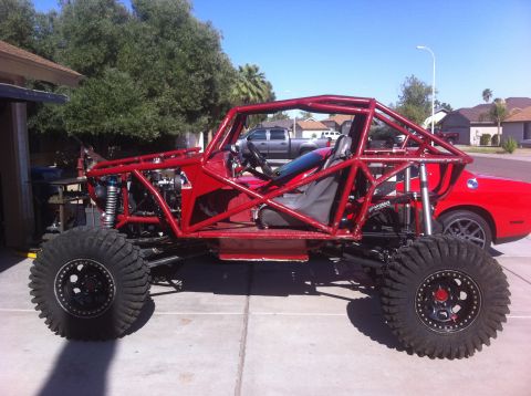 2009 Suzuki Samurai - A custom-built buggy with a prominent roll cage and off-road tires is shown from the side, with a red car in the background.