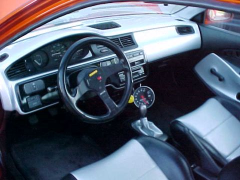 1999 Ford Taurus - The interior of a car shows an aftermarket steering wheel, a tachometer, and racing seats.