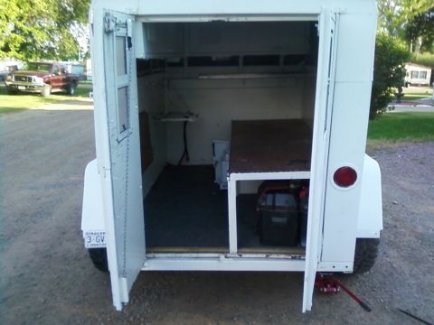 2006 Ford E350 - The trailer's rear doors are open, revealing its interior storage space and a generator. A pickup truck is visible in the background.