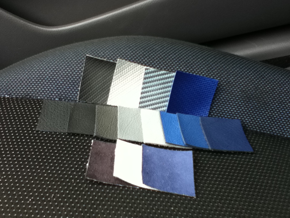 Interior fabric swatches on textured seat material. Swatches include various shades of gray, blue, and white