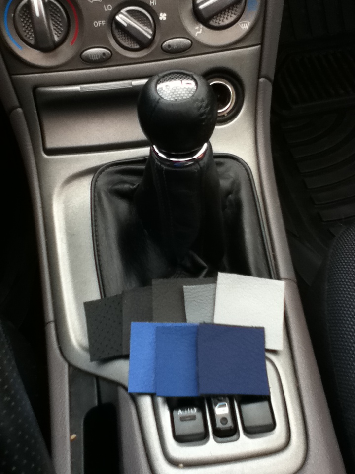 Car interior showing a black shift boot and samples of black, grey, and blue materials placed on the center console