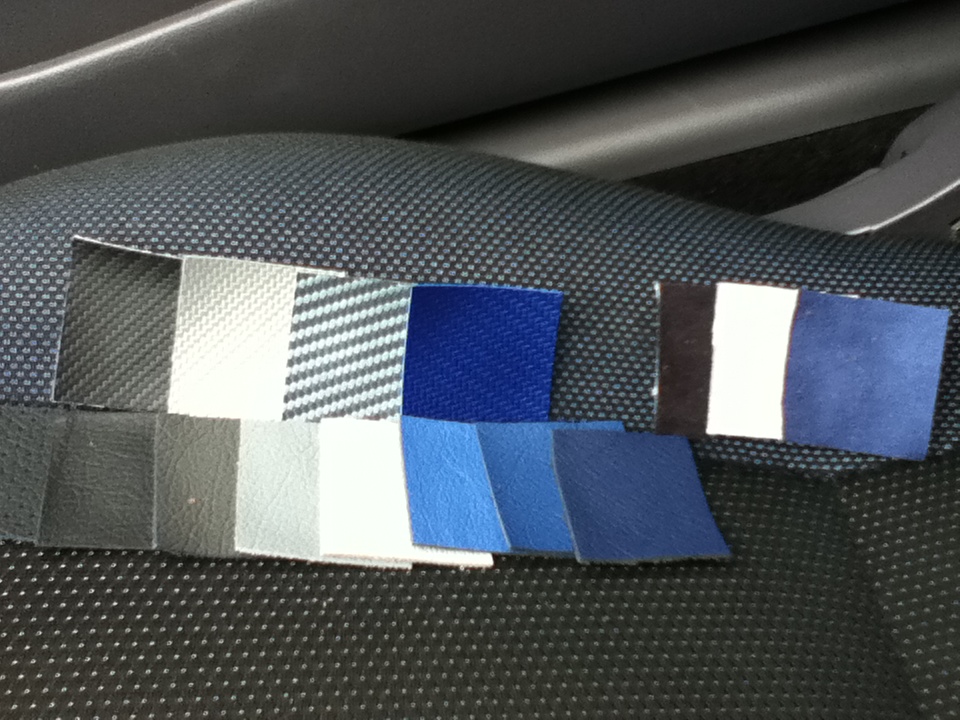 Various fabric and leather swatches in shades of blue, grey, and black laid out on a textured dark surface