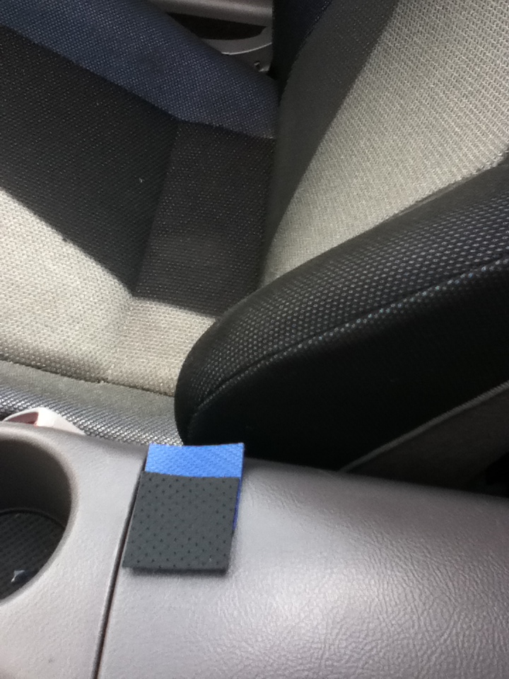Car interior close-up: gray center console with cup holder, cloth seats and small blue foam pad