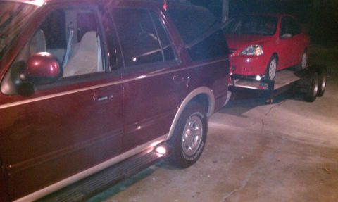 1999 Ford Expedition - A maroon Ford Expedition tows a red car on a trailer, with the Expedition's model year appearing to be around 1997.