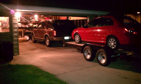 1999 Ford Expedition - A 1999 Ford Expedition is seen from the rear 3/4 angle, towing a red car on a trailer into a garage.