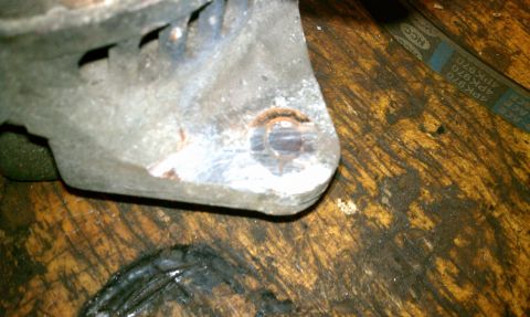 1999 Ford Expedition - Close-up of a rusty alternator bracket on a wooden workbench, with a drive belt in the background.