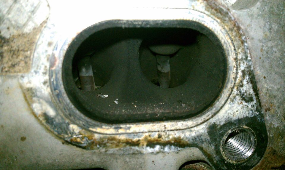 Engine cylinder head with two intake ports, covered in carbon buildup and rust