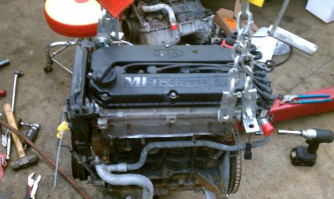 1999 Ford Expedition - Engine with KIA branding and V6 DOHC 16V text is suspended by chains in a workshop.