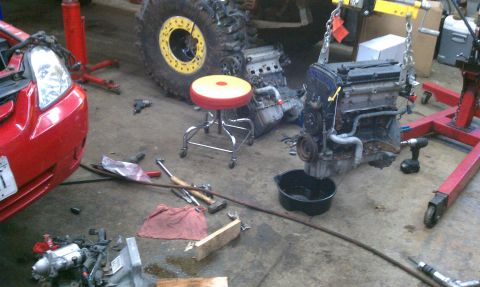 1999 Ford Expedition - An engine is suspended on a red stand in a workshop, with tools and other vehicle parts scattered around.