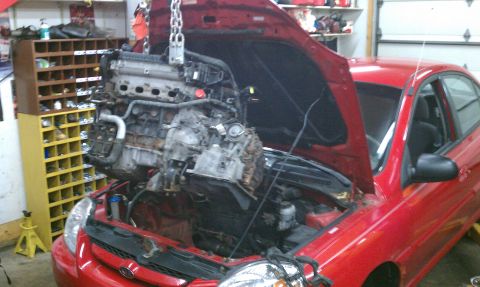 1999 Ford Expedition - The engine is being removed from a red car in a garage setting with a parts organizer in the background.