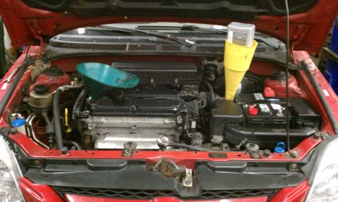 1999 Ford Expedition - Engine bay with a teal funnel and a yellow funnel with a gauge, suggesting an oil change is in progress.