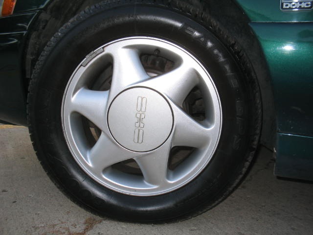 Close-up of a silver 5-spoke wheel with a "SAAB" center cap on a dark green car