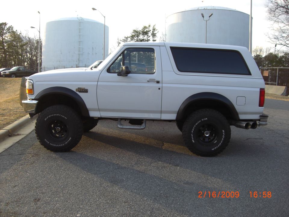 White 1996 Ford Bronco parked outside with large tanks in background