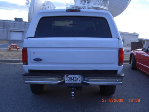 1996 Ford Bronco - Rear view of a white 1996 Ford Bronco, showing its license plate and a red sports car parked nearby.