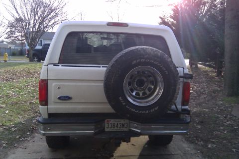 1996 Ford Bronco - The rear of a white Ford Bronco is shown with a spare tire mounted externally. A license plate is visible below the tire.
