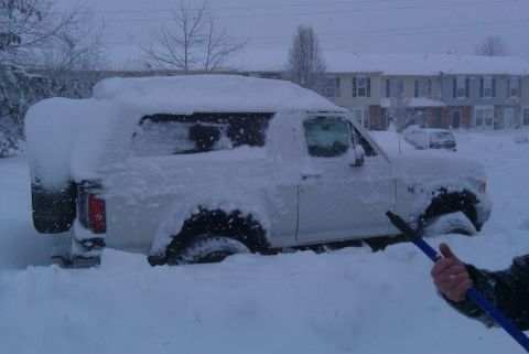 1996 Ford Bronco - A white SUV is heavily covered in snow, with a second vehicle barely visible in the distance.
