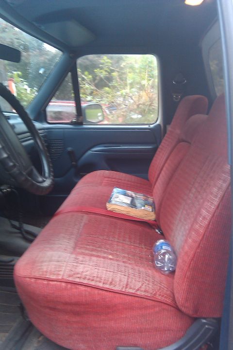 1996 Ford Bronco - The interior of a truck features a red bench seat and a view through the side window.