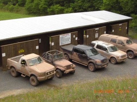 1996 Ford Bronco - Multiple muddy trucks and SUVs are parked in front of a barn.