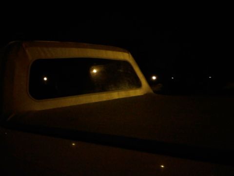 1996 Ford Bronco - The rear window of a vehicle with a soft top is visible at night, with reflections in the glass.