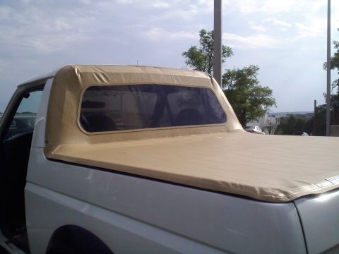 1996 Ford Bronco - A white Ford truck fitted with a tan/beige soft top and matching soft tonneau cover over the bed, with a tinted rear window, shown from a r…