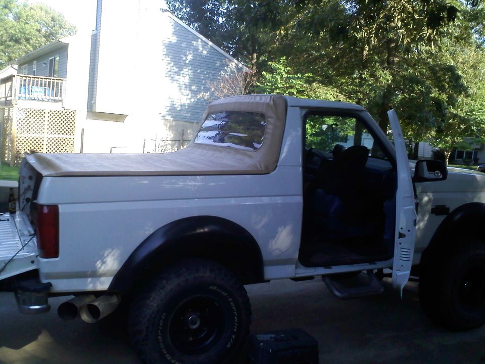 White 1992-96 full-size Ford Bronco with tan soft top and door open parked in a yard