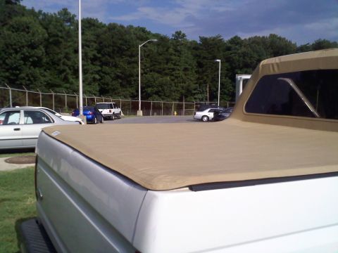 1996 Ford Bronco - Rear view of a 1996 Ford Bronco a tan soft top, with other vehicles in the background.