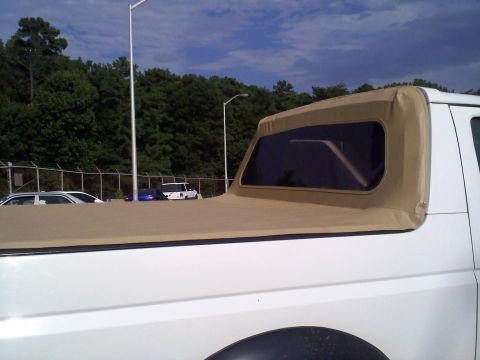 1996 Ford Bronco - A white Ford Bronco with a tan soft top is parked outdoors, with other vehicles visible in the background.