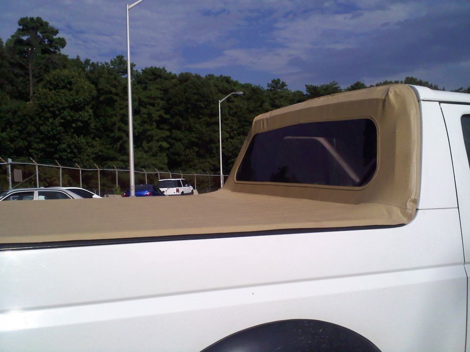 White Ford Bronco with a tan soft top, parked near other cars