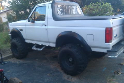 1996 Ford Bronco - This white Ford Bronco features a black soft top and is lifted with large off-road tires.