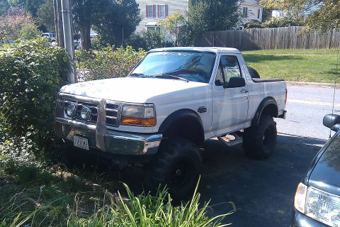 1996 Ford Bronco - This lifted Ford Bronco is parked in a residential area, partially obscured by bushes.