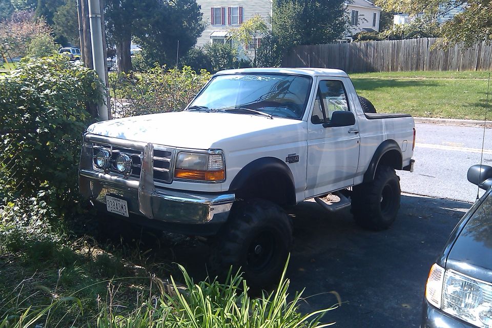 Lifted white Ford Bronco parked on a driveway, front end visible