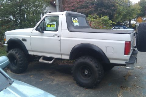 1996 Ford Bronco - White 1990s Ford Bronco shown from the driver's side, lifted on black steel wheels with large mud-terrain tires, black removable hardtop, t…