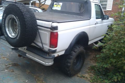 1996 Ford Bronco - Rear three-quarter view of a white full-size Ford Bronco with its hardtop removed, running a soft top over the cab and a black cover over t…