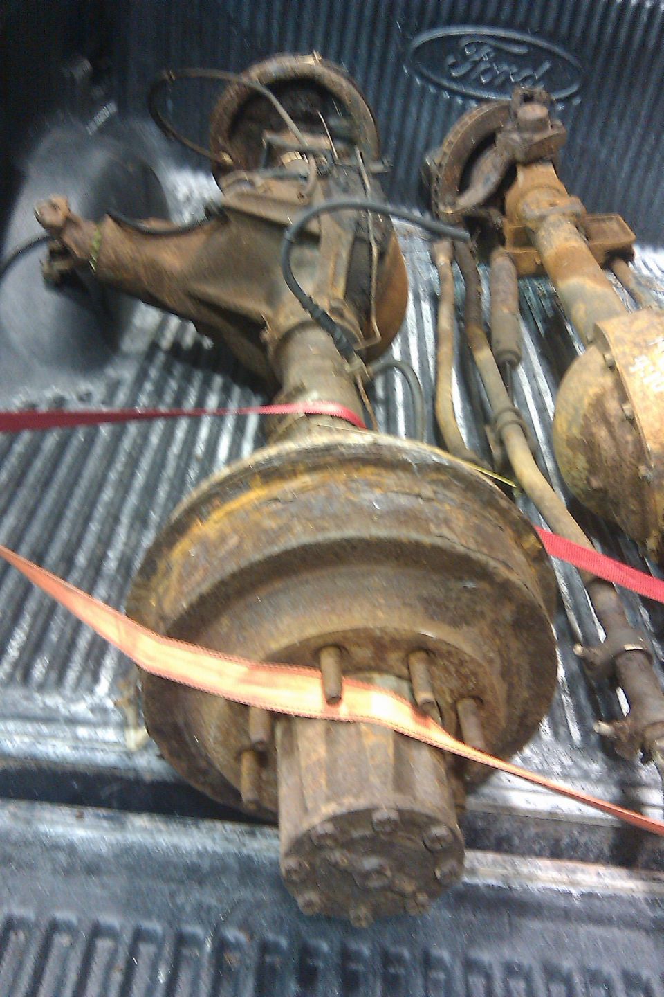 Two rusty Ford rear axles in a truck bed. Ford logo visible