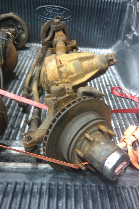 1996 Ford Bronco - Rusted Ford Bronco front axle assembly with brake rotor and hub is loaded in a truck bed.
