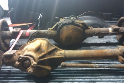1996 Ford Bronco - Two heavily rusted truck axles are secured with straps in the bed of a pickup truck.