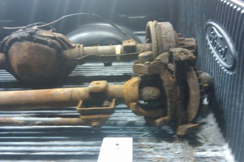 1996 Ford Bronco - Two heavily rusted rear axles are loaded into the bed of a truck, with a Ford emblem on the tailgate.