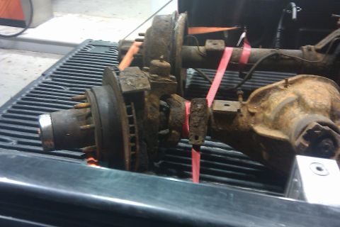 1996 Ford Bronco - Two heavily rusted axles, likely from a truck or SUV, are secured with straps in the bed of a pickup.