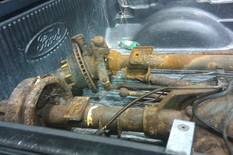 1996 Ford Bronco - Two heavily rusted vehicle axles are loaded into the bed of a Ford pickup truck.