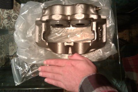 1996 Ford Bronco - A single brake caliper is shown in its packaging, with a hand obscuring part of the view.