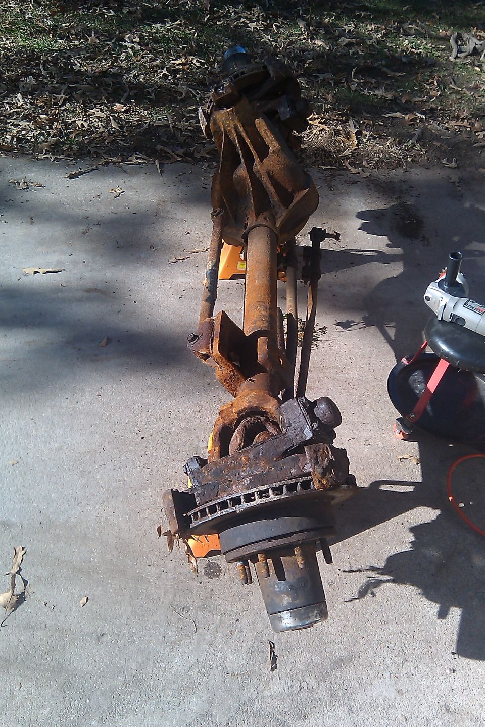 rusted front axle assembly with brake rotor and hub, resting on concrete