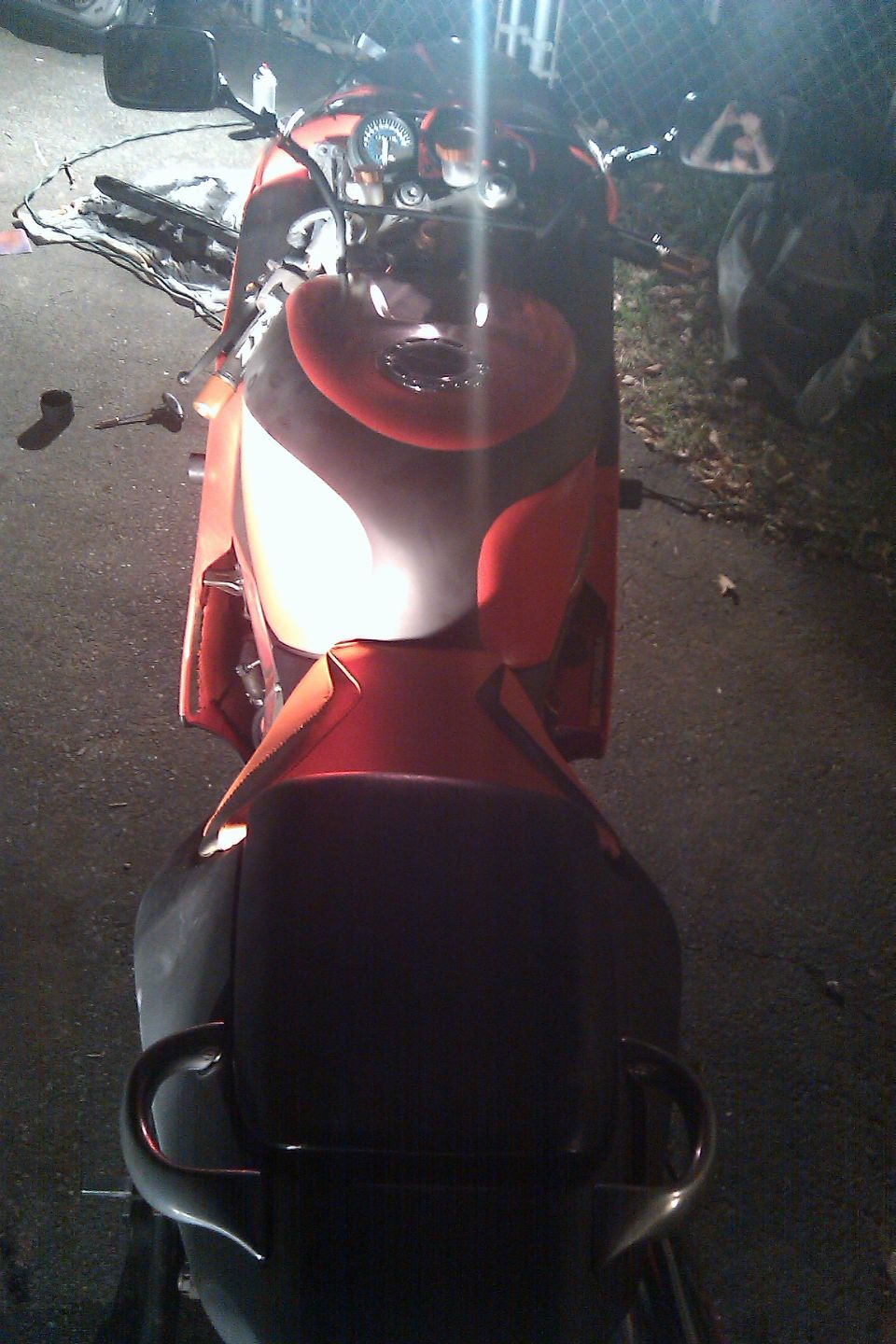 Motorcycle fuel tank and seat, red and black colors. Handlebars and gauge visible