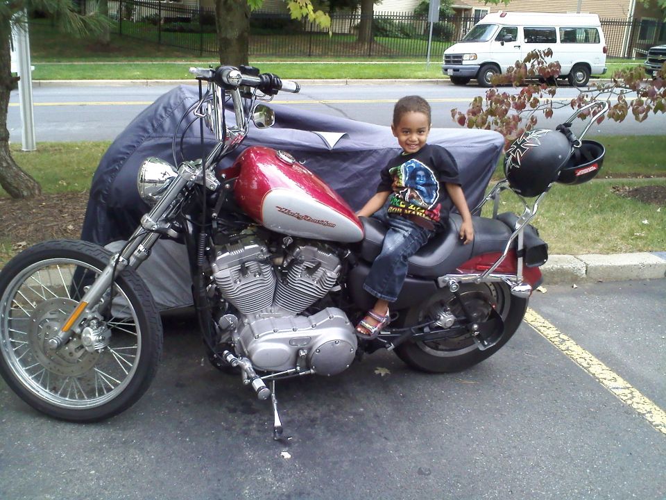 Child sits on a red and silver 2004 Harley-Davidson Sportster Custom motorcycle parked outdoors