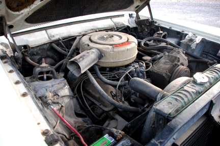 1965 Ford Fairlane - The engine compartment of a vintage automobile is shown with its hood open, revealing the motor and associated components.