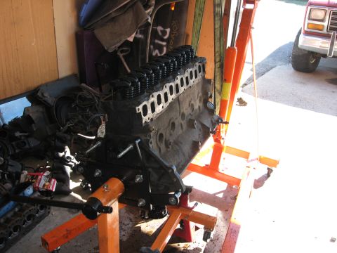 1981 Ford Bronco - An engine is mounted on an orange engine stand, with a red Ford truck visible in the background.