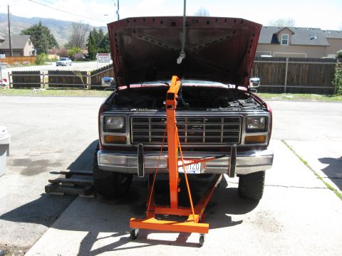 1981 Ford Bronco - A red pickup truck is parked outside with its hood up and an engine hoist positioned in front of it.
